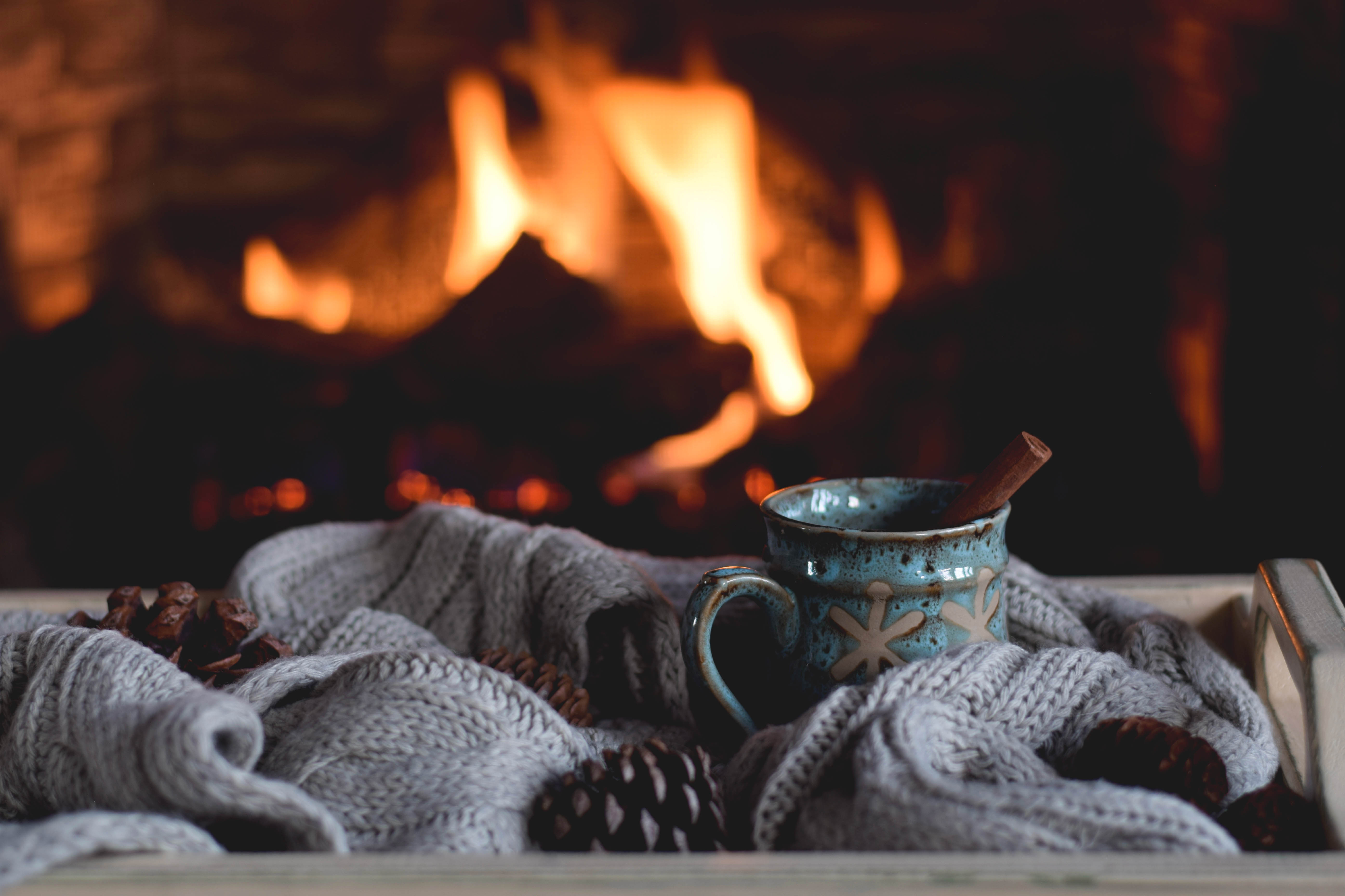 Close-up of a fireplace with a mug of hot cocoa with a cinnamon stick and a cozy blanket